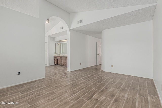 6701 W Monterey Way, Phoenix, AZ 85033 - unfurnished living room featuring wood finished floors, a textured ceiling, high vaulted ceiling, baseboards, and arched walkways