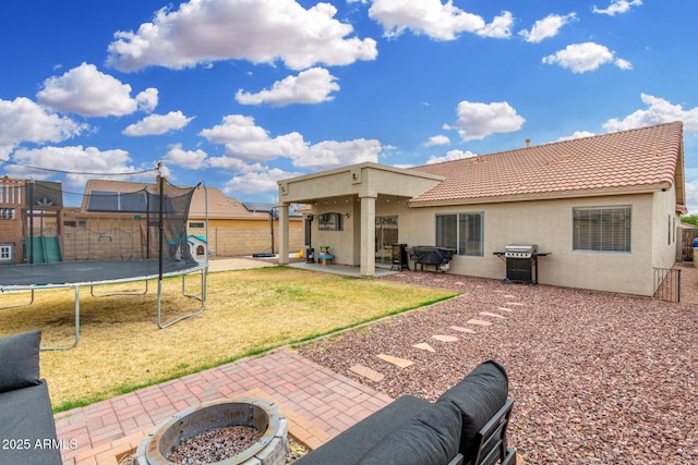 rear view of house featuring a patio, stucco siding, a fire pit, a tile roof, and a trampoline