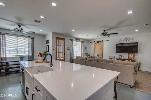 kitchen with concrete floors, a barn door, a breakfast bar area, a kitchen island with sink, and white cabinetry