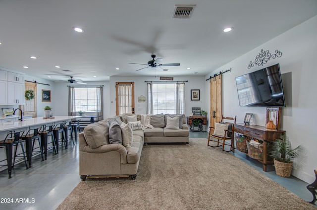 living room featuring concrete flooring, a barn door, and ceiling fan