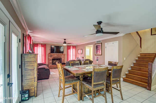 tiled dining area featuring crown molding, ceiling fan, and a brick fireplace