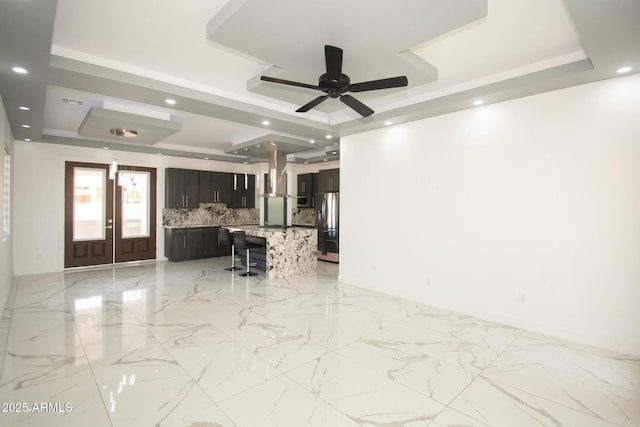 unfurnished living room featuring ceiling fan and a raised ceiling