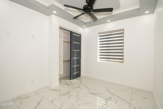 unfurnished bedroom with ceiling fan, a spacious closet, a tray ceiling, and a closet