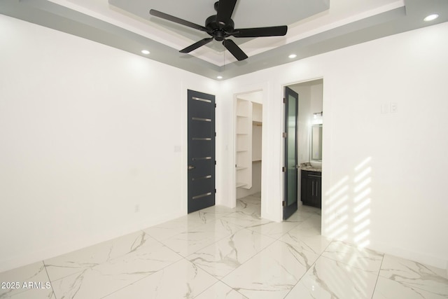 unfurnished bedroom featuring a raised ceiling, ceiling fan, a spacious closet, connected bathroom, and a closet