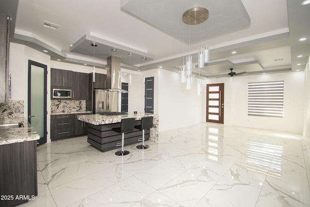 kitchen featuring a raised ceiling, decorative light fixtures, island exhaust hood, and stainless steel appliances