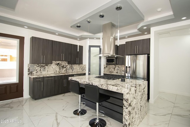 kitchen with tasteful backsplash, island range hood, light stone counters, and hanging light fixtures