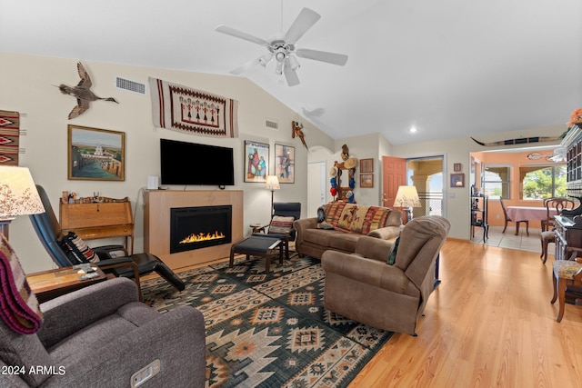 living room with light wood-type flooring, ceiling fan, lofted ceiling, and a fireplace