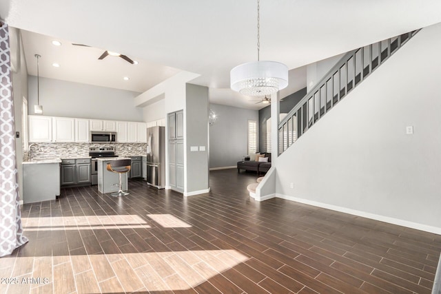 kitchen with open floor plan, ceiling fan with notable chandelier, stainless steel appliances, and wood tiled floor