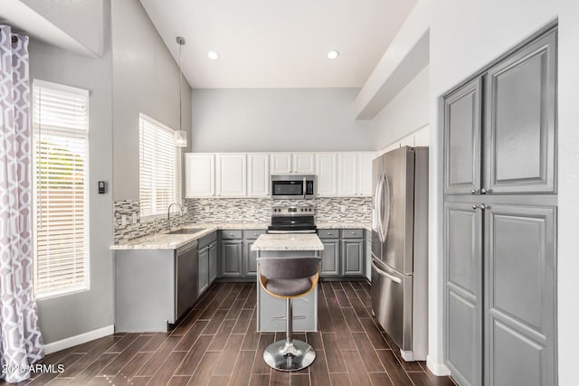 kitchen featuring a kitchen island, a sink, decorative backsplash, gray cabinetry, and appliances with stainless steel finishes