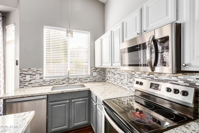 kitchen featuring light stone countertops, gray cabinetry, decorative backsplash, a sink, and appliances with stainless steel finishes