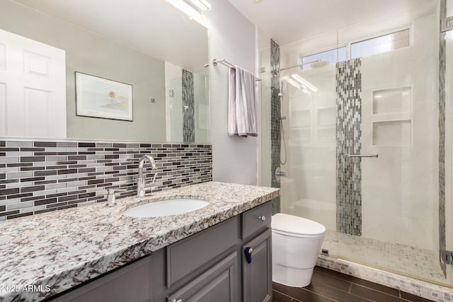 bathroom with backsplash, a shower stall, toilet, wood finished floors, and vanity