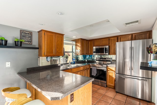 kitchen featuring kitchen peninsula, light tile patterned floors, appliances with stainless steel finishes, a breakfast bar, and sink