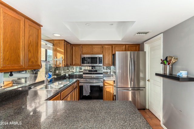 kitchen with kitchen peninsula, tasteful backsplash, a raised ceiling, appliances with stainless steel finishes, and sink