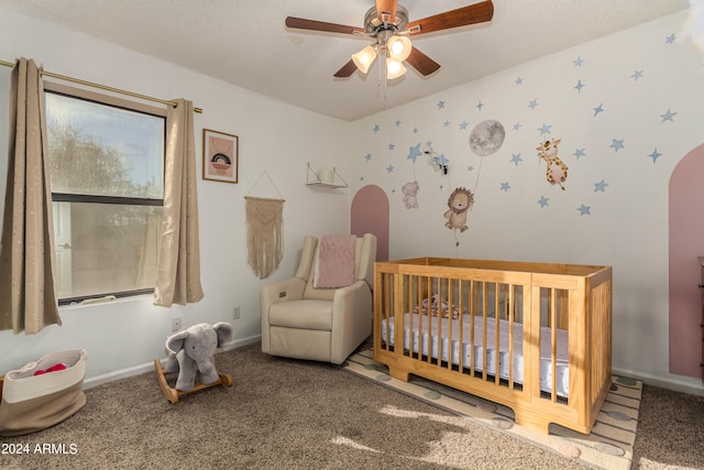 carpeted bedroom with ceiling fan, a textured ceiling, and a nursery area