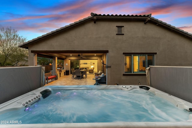 back house at dusk featuring area for grilling, ceiling fan, a patio, and a hot tub