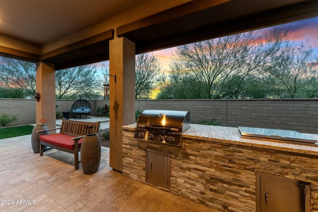 patio terrace at dusk featuring exterior kitchen and a grill