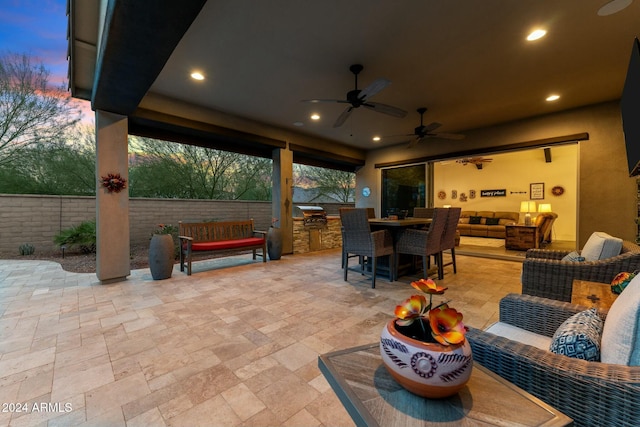 patio terrace at dusk with an outdoor living space, ceiling fan, and exterior kitchen