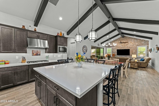 kitchen featuring a breakfast bar, stainless steel microwave, beamed ceiling, dark brown cabinets, and a kitchen island