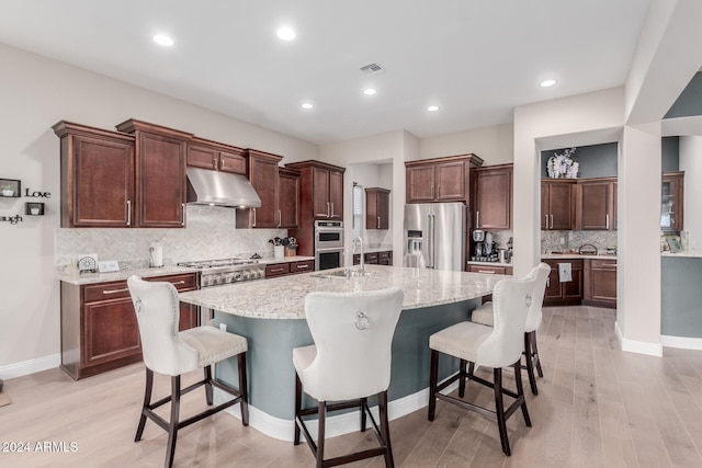 kitchen featuring a breakfast bar, appliances with stainless steel finishes, a center island with sink, and light hardwood / wood-style flooring