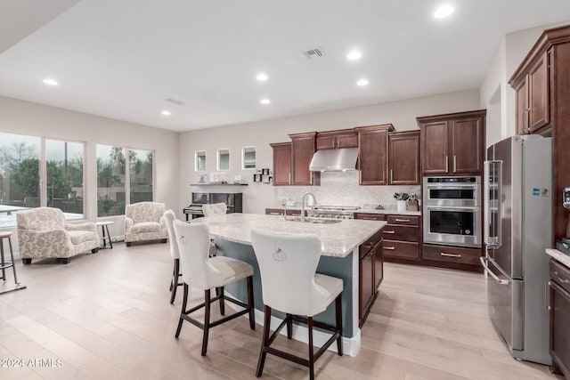 kitchen featuring a center island with sink, sink, appliances with stainless steel finishes, tasteful backsplash, and light stone counters