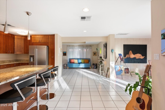 kitchen with light tile patterned floors, visible vents, open floor plan, brown cabinets, and stainless steel fridge