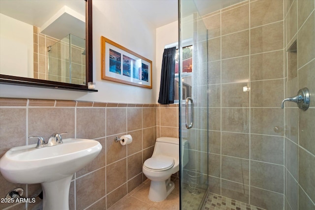 bathroom with tile patterned flooring, toilet, tile walls, wainscoting, and a shower stall