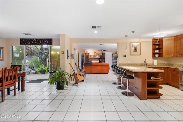 kitchen with open shelves, brown cabinetry, open floor plan, a sink, and light stone countertops