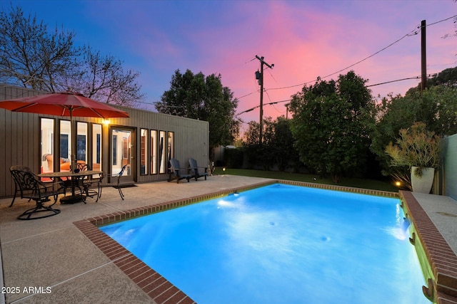 pool at dusk with a patio area and an outdoor pool