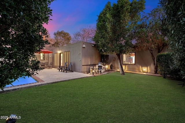 back of house at dusk with fence, a patio, and a yard