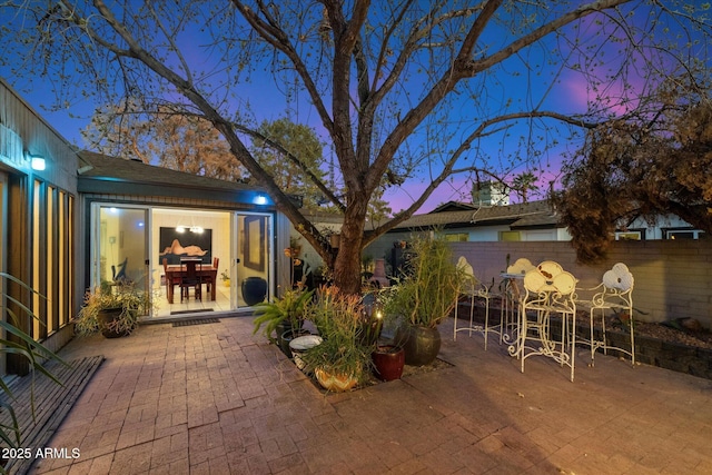 patio terrace at dusk featuring outdoor dining area and fence