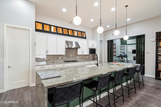 kitchen with a large island with sink, built in microwave, tasteful backsplash, gas stovetop, and under cabinet range hood