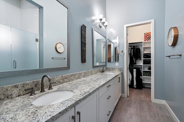 full bath with a walk in closet, double vanity, baseboards, and a sink