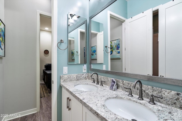 bathroom with baseboards, wood finished floors, a sink, and double vanity