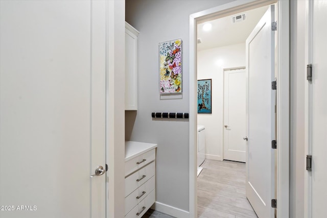 corridor with light wood finished floors, baseboards, visible vents, and washer / clothes dryer