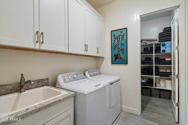 clothes washing area featuring a sink, baseboards, washer and dryer, cabinet space, and light wood-style flooring