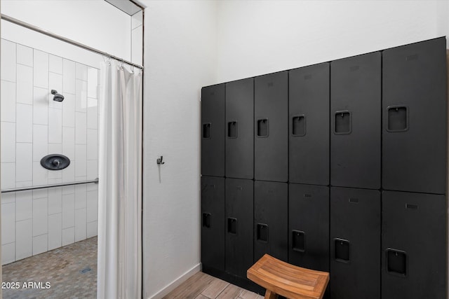 full bathroom featuring a tile shower, baseboards, and wood finished floors