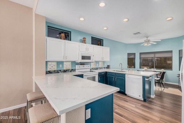 kitchen with sink, white appliances, a breakfast bar area, white cabinetry, and kitchen peninsula