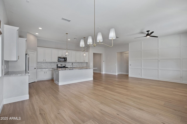 kitchen featuring an island with sink, pendant lighting, stainless steel appliances, decorative backsplash, and white cabinets