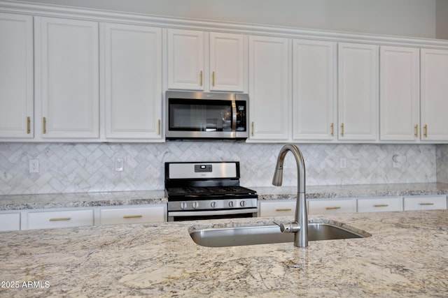 kitchen with tasteful backsplash, sink, white cabinets, stainless steel appliances, and light stone countertops