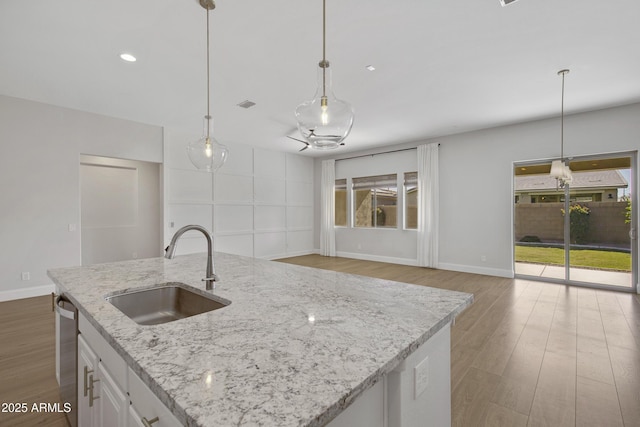 kitchen featuring decorative light fixtures, white cabinetry, sink, light stone countertops, and a center island with sink