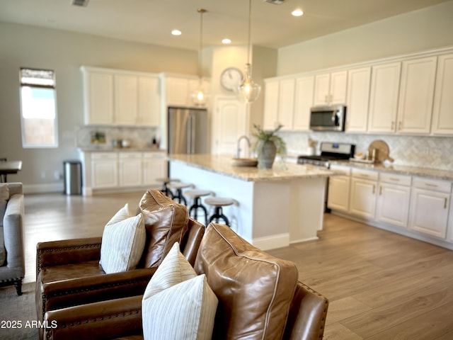 kitchen with decorative light fixtures, appliances with stainless steel finishes, a kitchen island, light stone countertops, and white cabinets