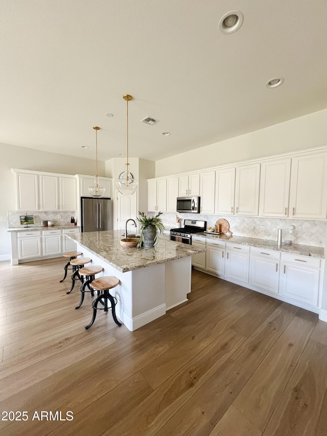 kitchen with stainless steel appliances, decorative light fixtures, a kitchen island with sink, and white cabinets