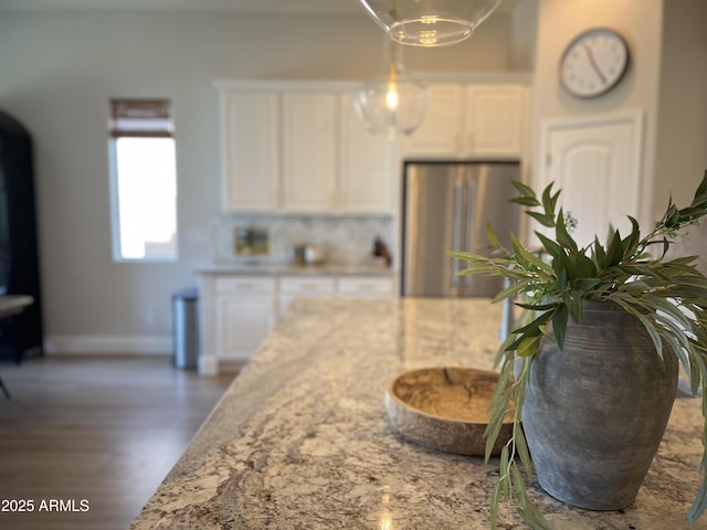 kitchen with stainless steel refrigerator, pendant lighting, light stone counters, and white cabinets