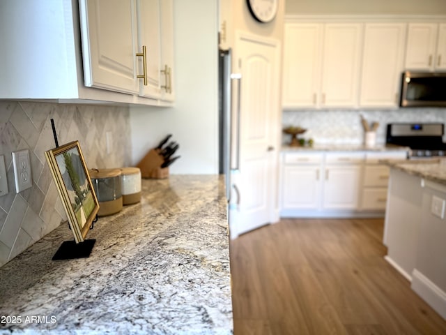 kitchen with white cabinets, backsplash, range, light stone countertops, and light wood-type flooring