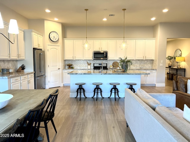 kitchen featuring appliances with stainless steel finishes, decorative light fixtures, white cabinets, a kitchen breakfast bar, and light stone countertops