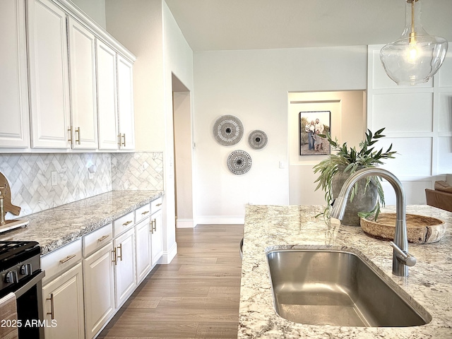 kitchen with sink, white cabinetry, light hardwood / wood-style flooring, pendant lighting, and decorative backsplash