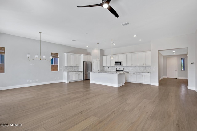 unfurnished living room with sink, ceiling fan with notable chandelier, and light wood-type flooring