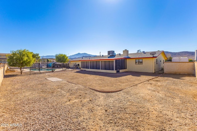 rear view of house with a mountain view, central AC unit, and a fenced in pool