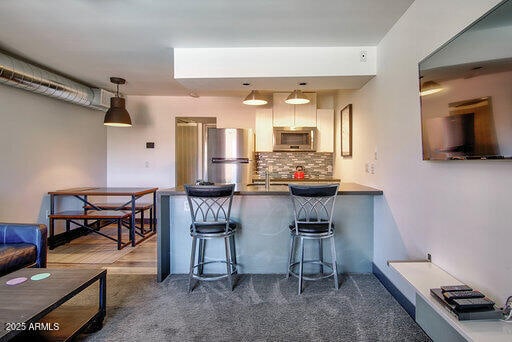 kitchen featuring appliances with stainless steel finishes, hanging light fixtures, a breakfast bar area, backsplash, and kitchen peninsula