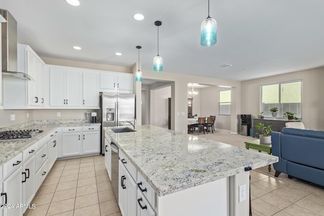 kitchen featuring appliances with stainless steel finishes, decorative light fixtures, wall chimney range hood, and an island with sink